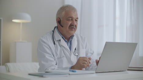 Ein-Fröhlicher-Männlicher-Arzt-Kommuniziert-Online-Mit-Kollegen-Oder-Patienten-Per-Laptop-Per-Videoanruf